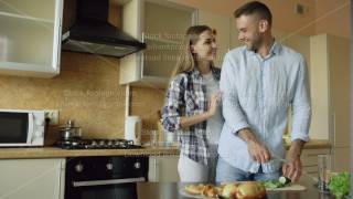 Happy young couple kissing embracing and chatting in the kitchen while cooking breakfast at home [upl. by Ruhtua]